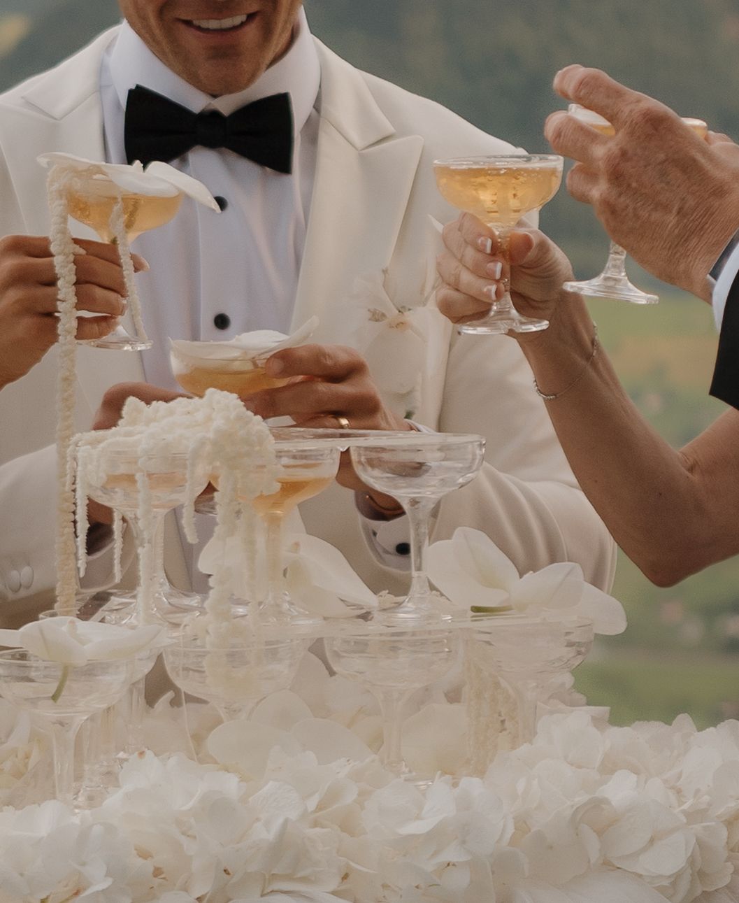 Wedding guests clinking champagne glasses over a floral display with mountain views in the background.