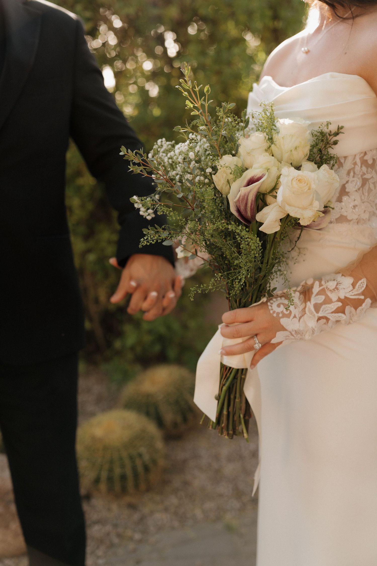 Bride holding white rose bouquet with ribbon while groom holds her hand in garden setting.