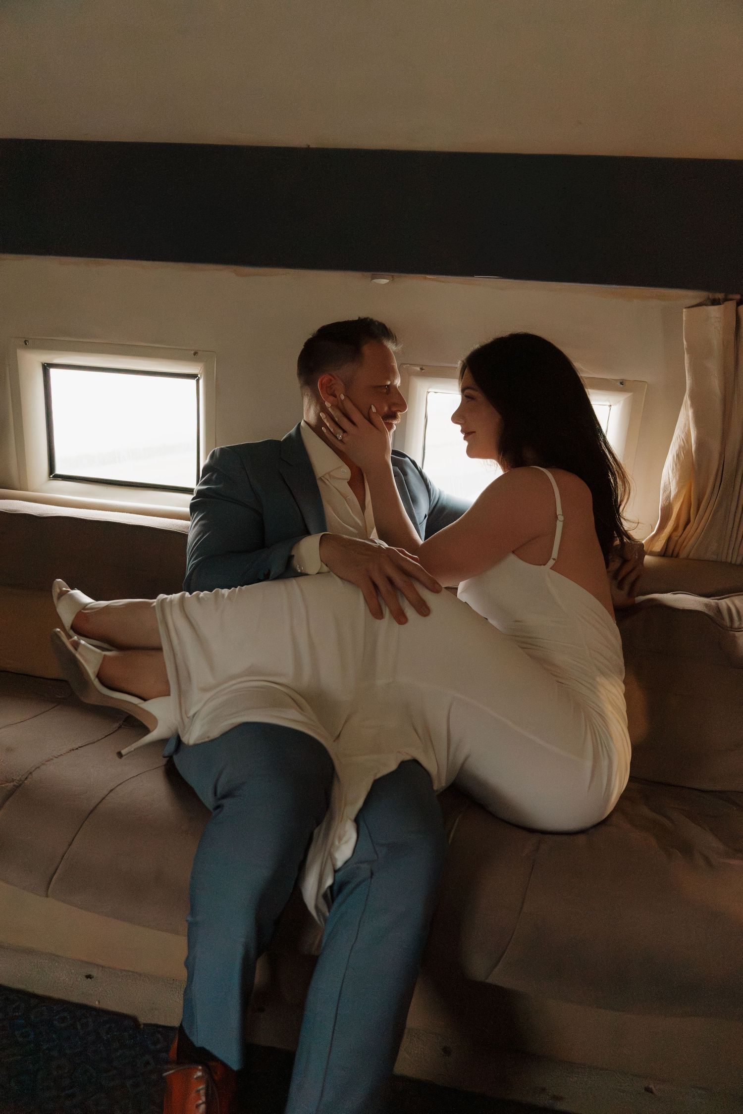 A couple in formal attire shares an intimate moment on a couch inside a private jet cabin.