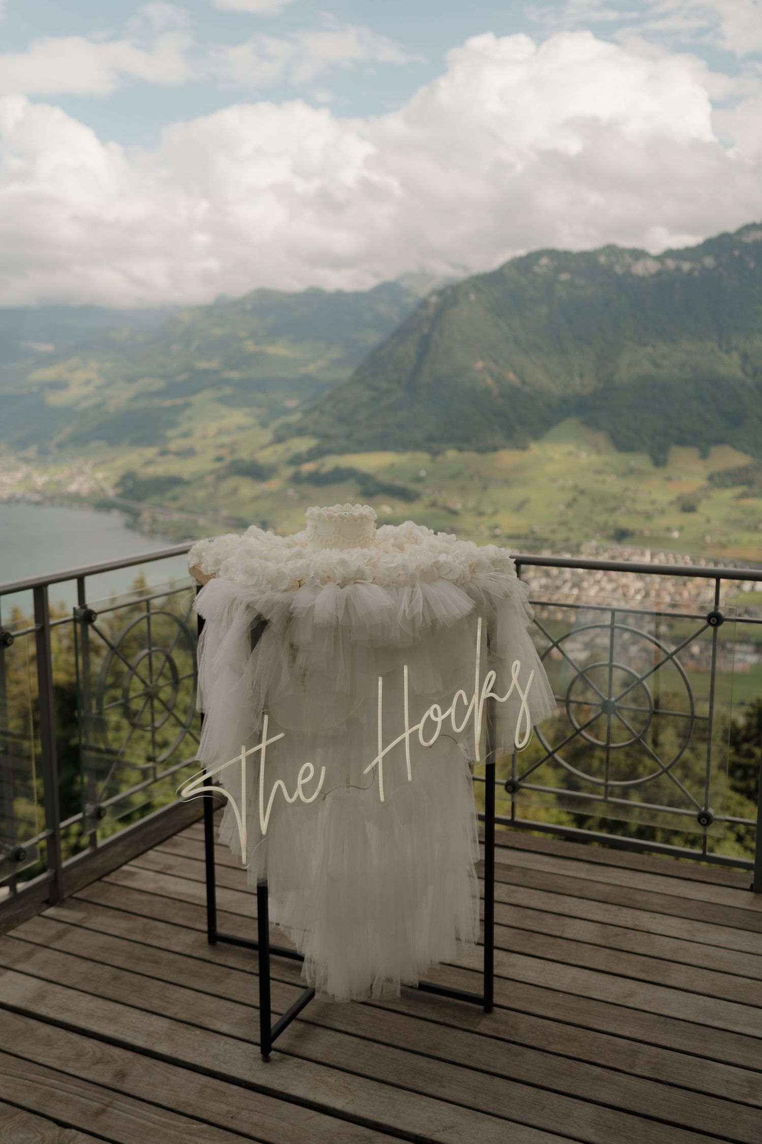 Wedding veil and decor displayed on chair on wooden terrace with alpine lake backdrop.
