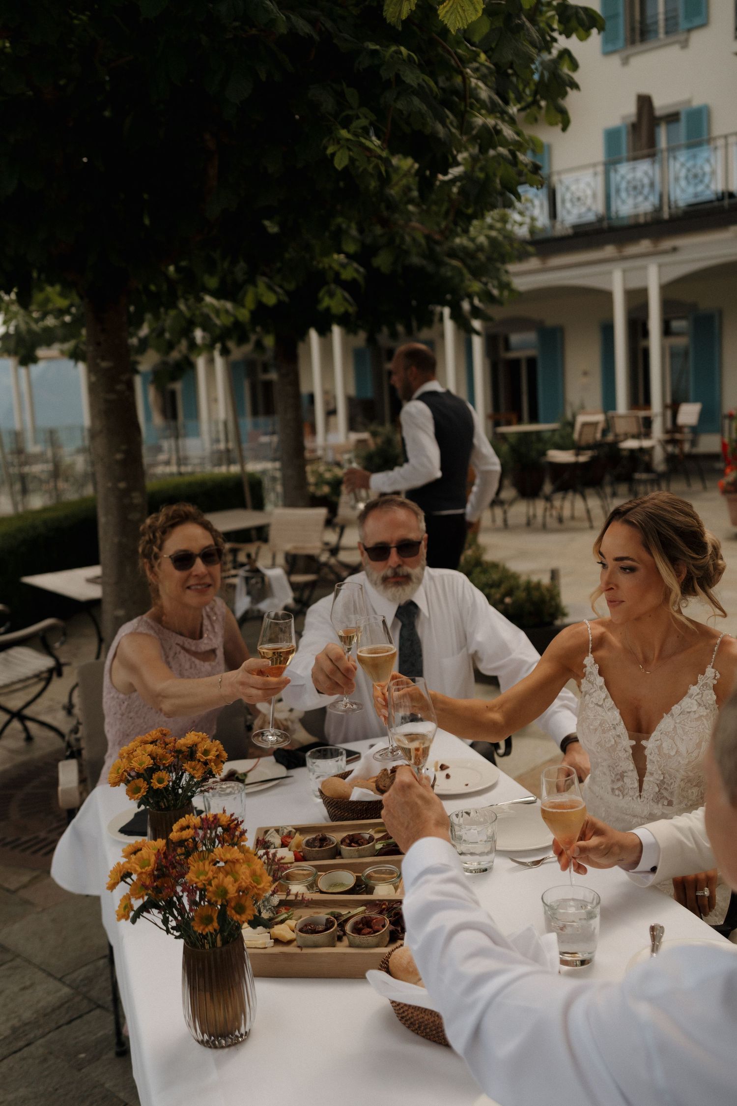 Bride toasts champagne with family at an outdoor wedding reception at a lakeside hotel.