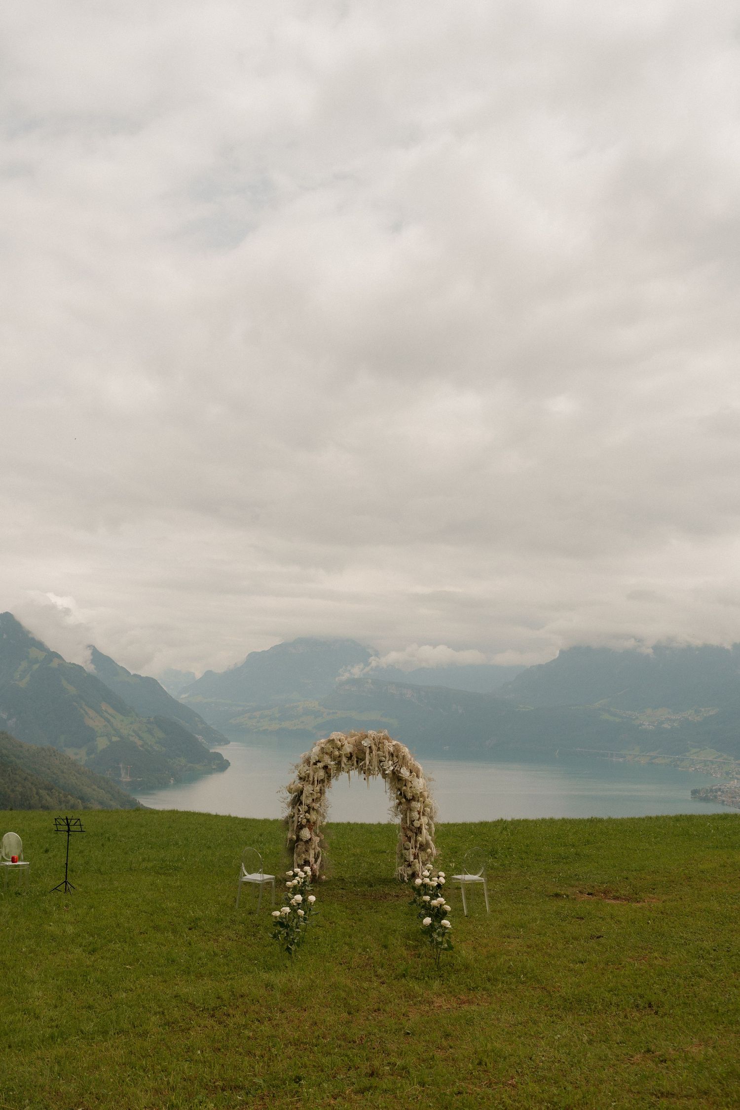 Elegant floral wedding arch on green hillside overlooking a serene alpine lake with mountain views.