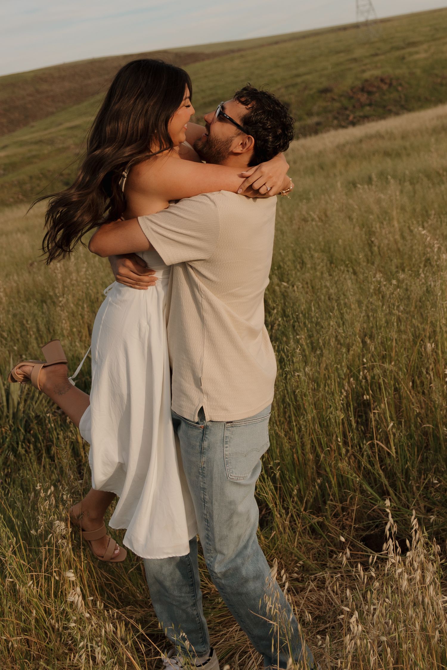 Couple embracing and kissing in golden hour sunlight in a green grassy field.