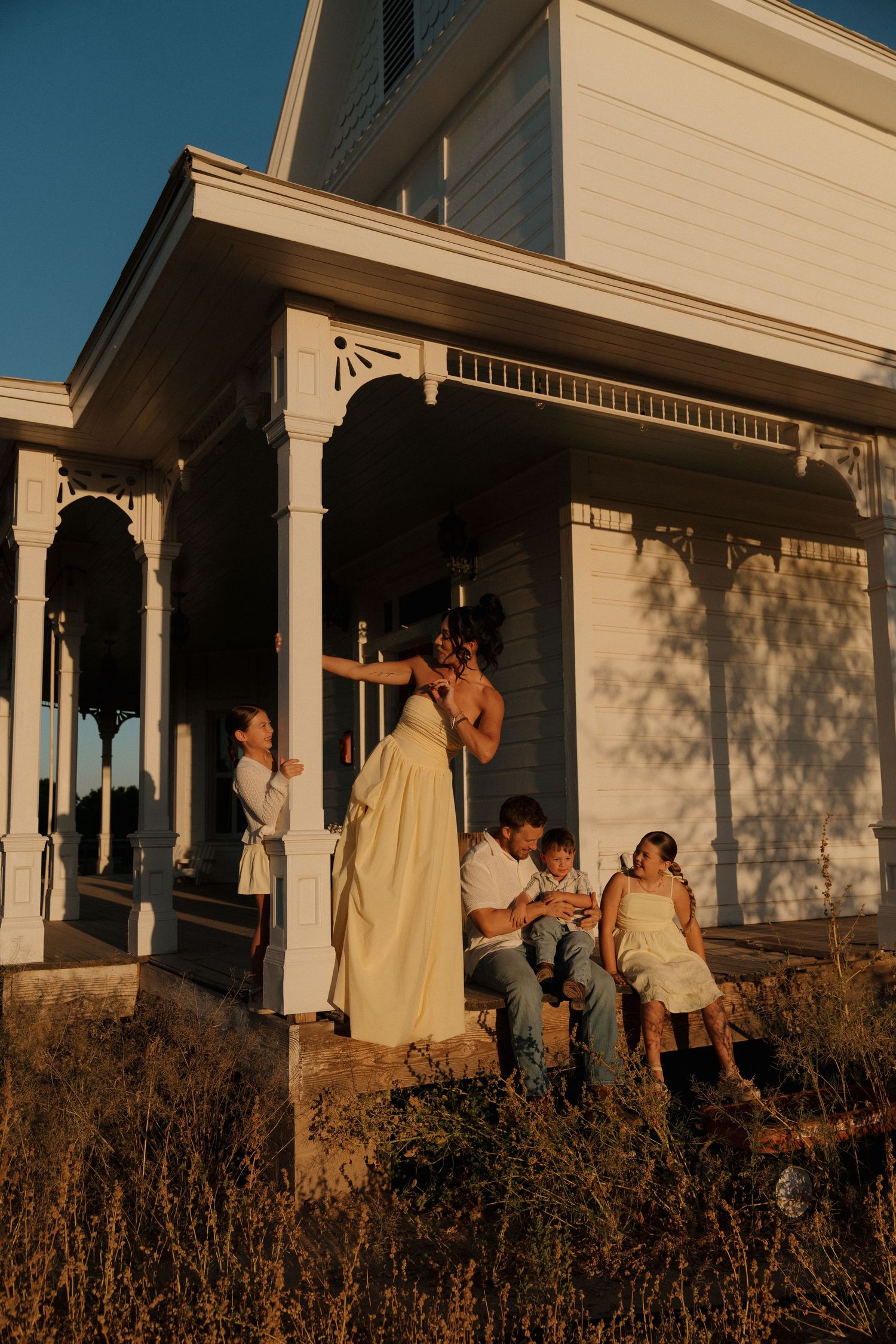 Family gathering on vintage white porch steps during warm golden hour sunset light in queen creek, arizona.