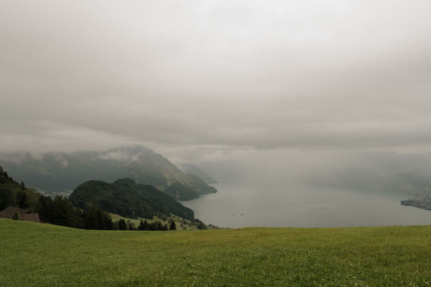 Misty overcast view of Swiss alpine lake surrounded by green hills and mountains.