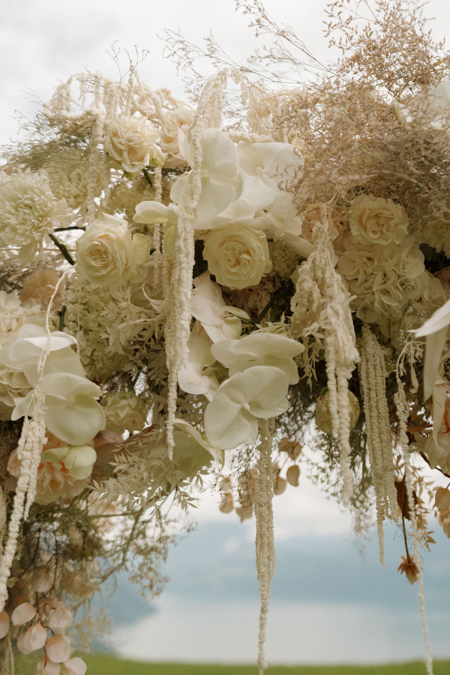 Detailed view of a whimsical wedding arch featuring white roses, orchids, and dried floral arrangements.
