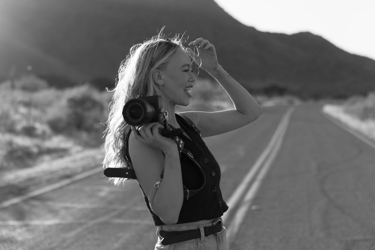 Woman holding camera on desert road in black and white photography portrait.