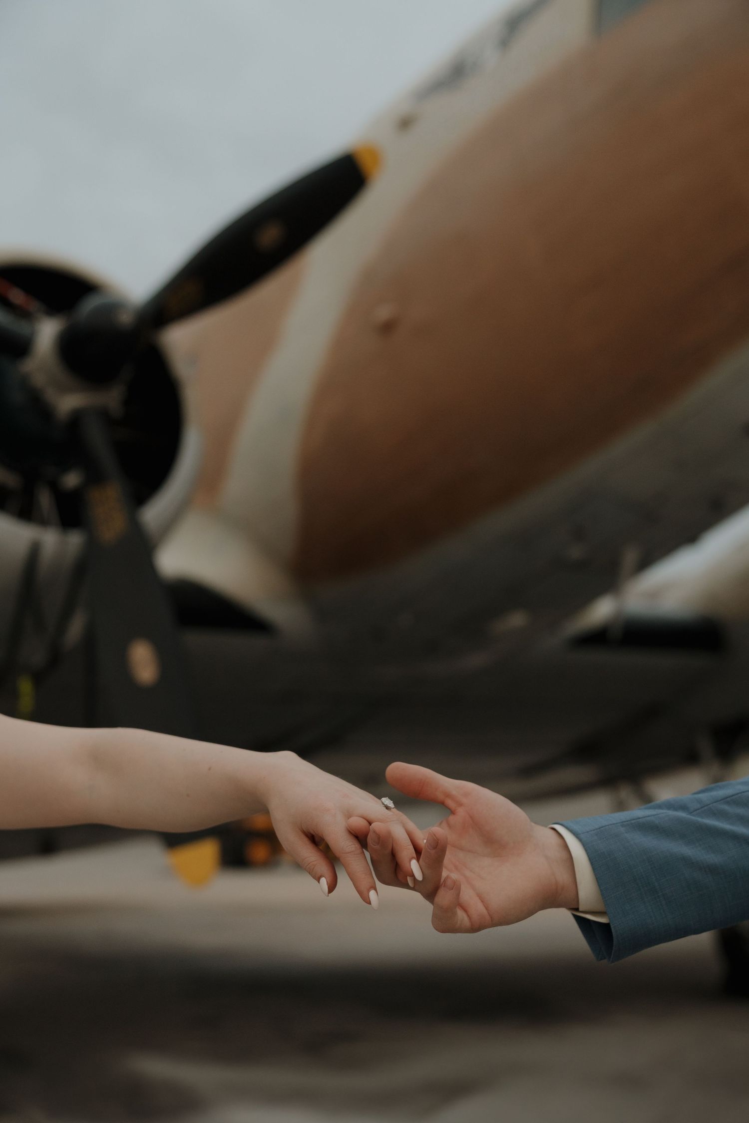 Two hands almost touching in front of a vintage propeller aircraft, evoking a romantic farewell scene.