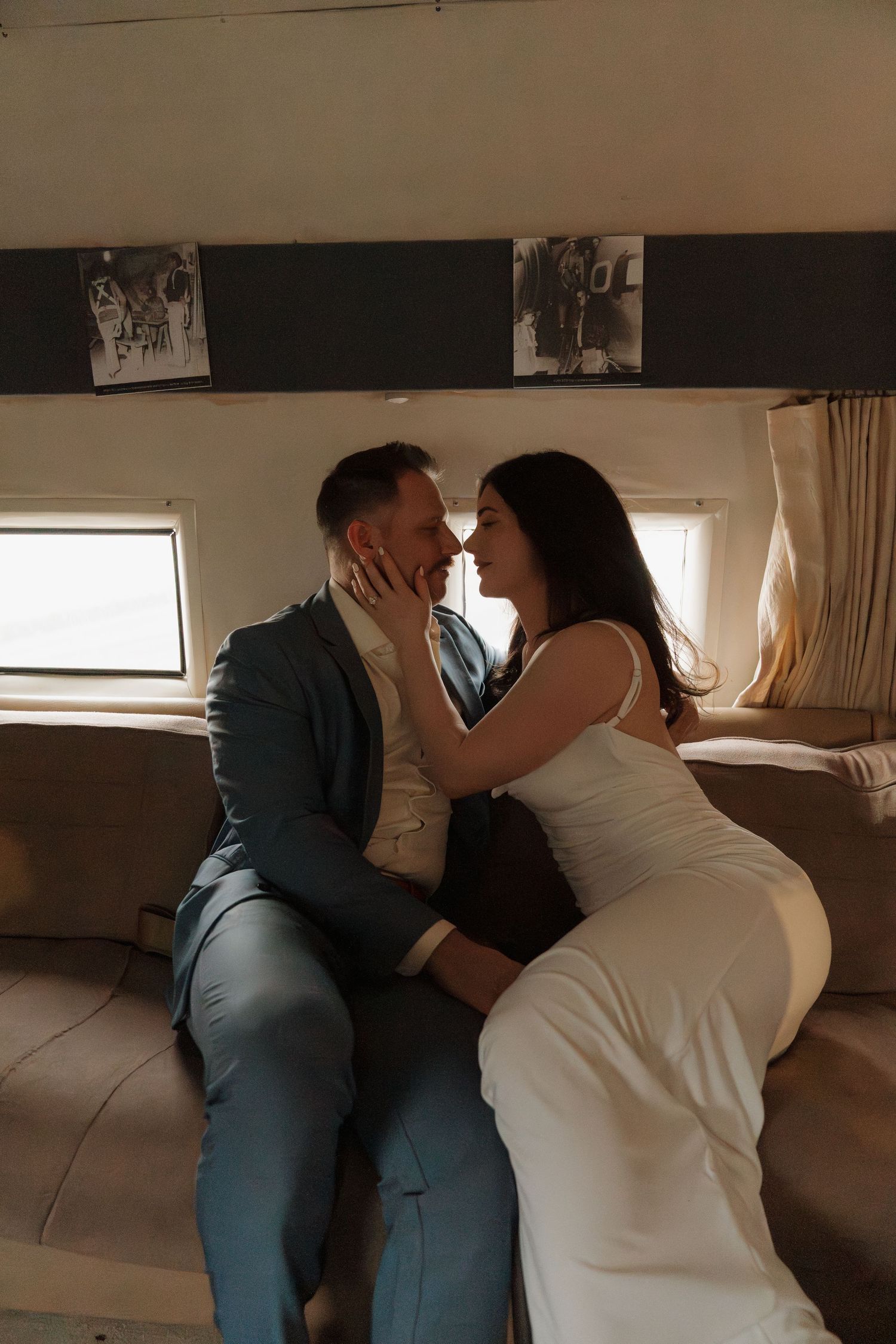 Romantic couple sharing an intimate moment on a private jet, woman in white dress cupping mans face.