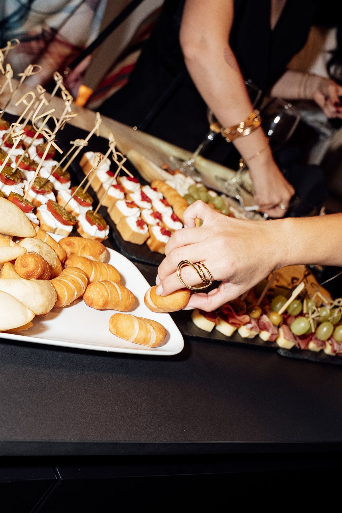 Hands reaching for appetizers and finger foods at an upscale catered event buffet table.