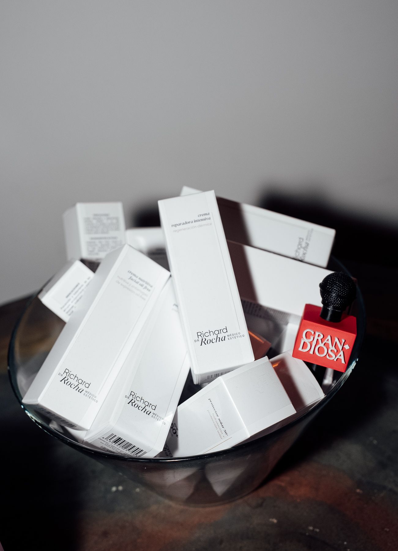 A glass bowl filled with white Richard Rocha skincare product boxes and a red Grandiosa tag at an event.