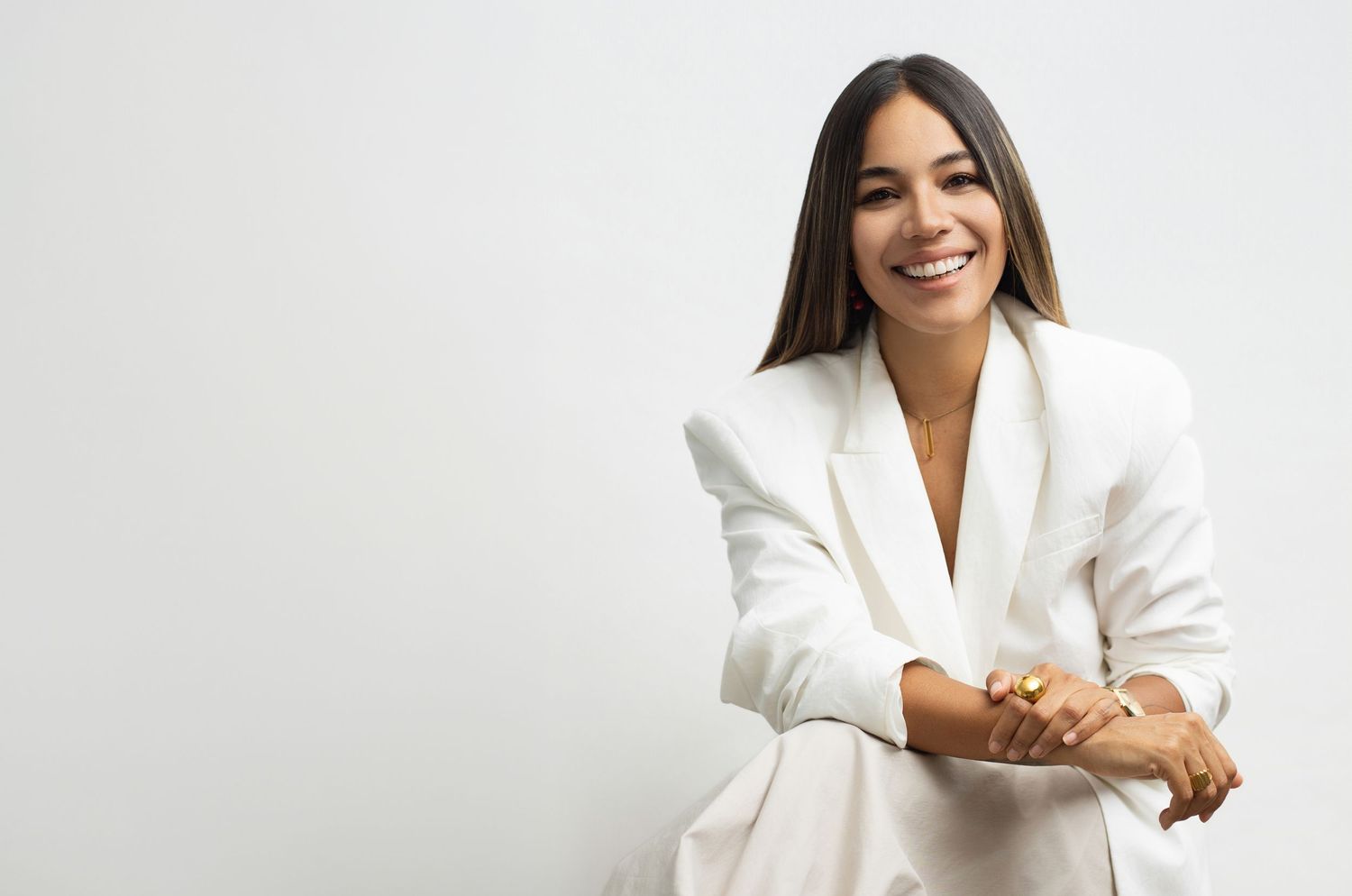 Smiling woman in white blazer poses confidently against light gray background with arms crossed.