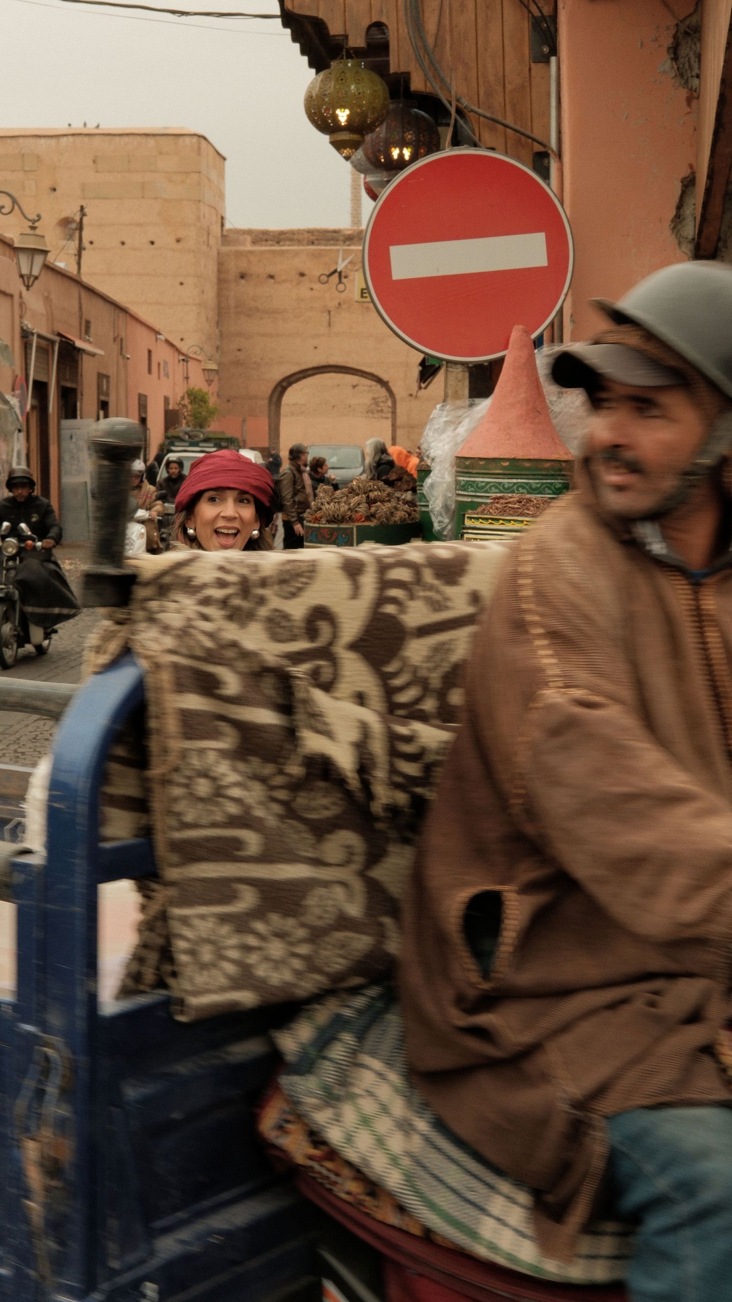 Busy Moroccan street scene with a man on a cart, a woman in a red hat, and a no-entry sign in the background.