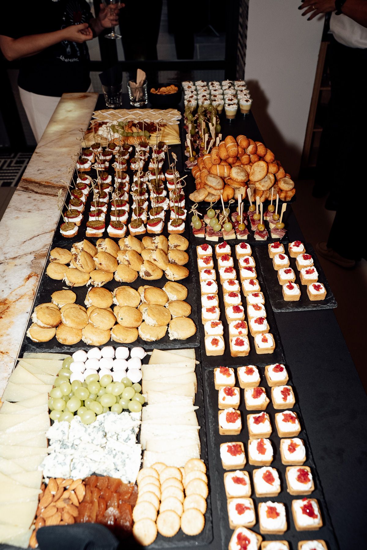 Elegant catering display with assorted canapes, mini burgers, pastries, and fresh fruit at an event.