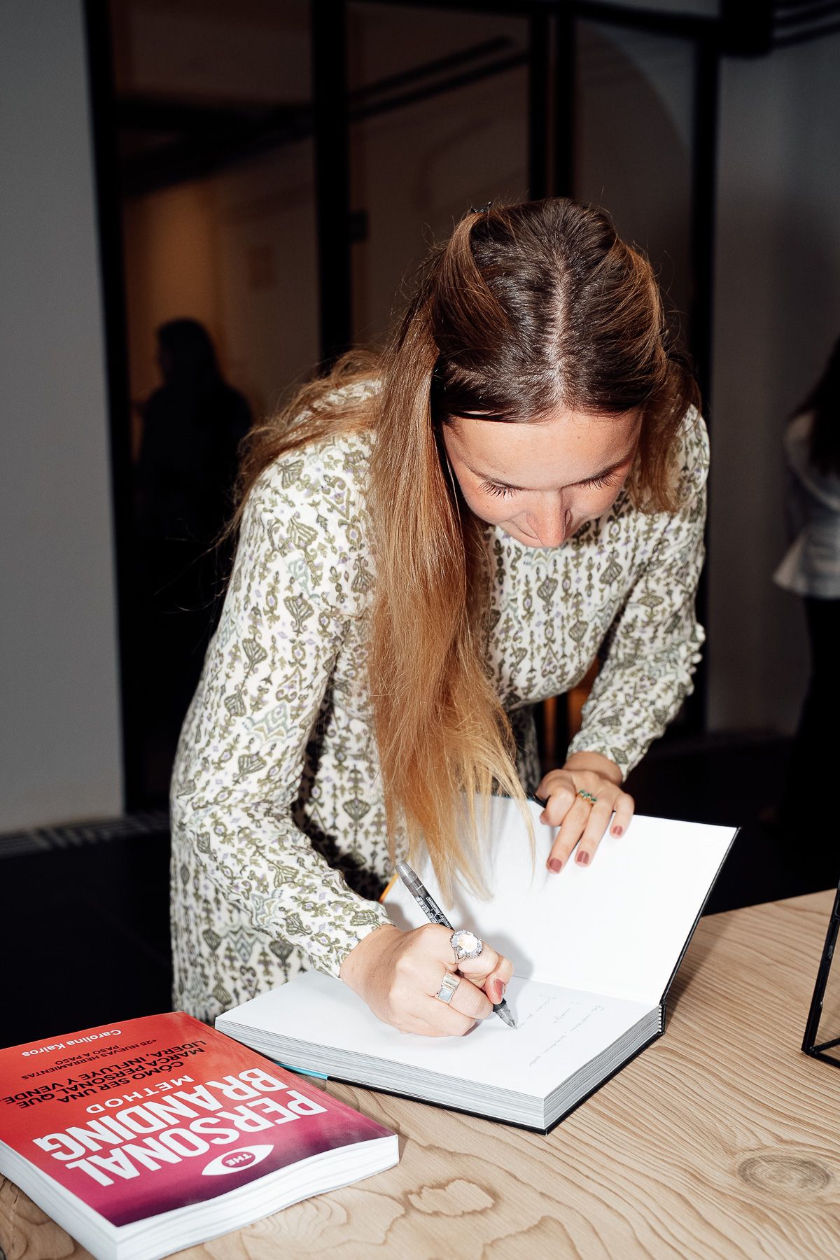 Woman in knit sweater signing a Personal Branding book at a wooden table during a book signing event.