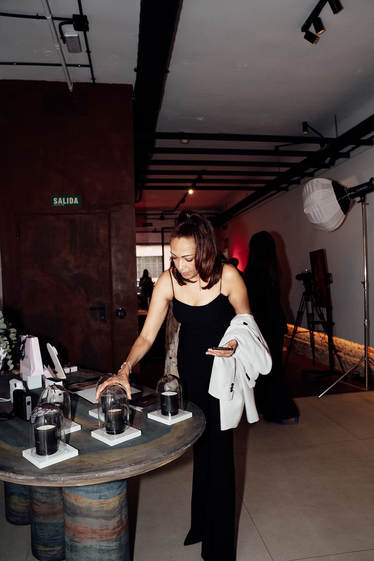 Elegant woman in black dress browsing jewelry displays at an upscale indoor brand event.