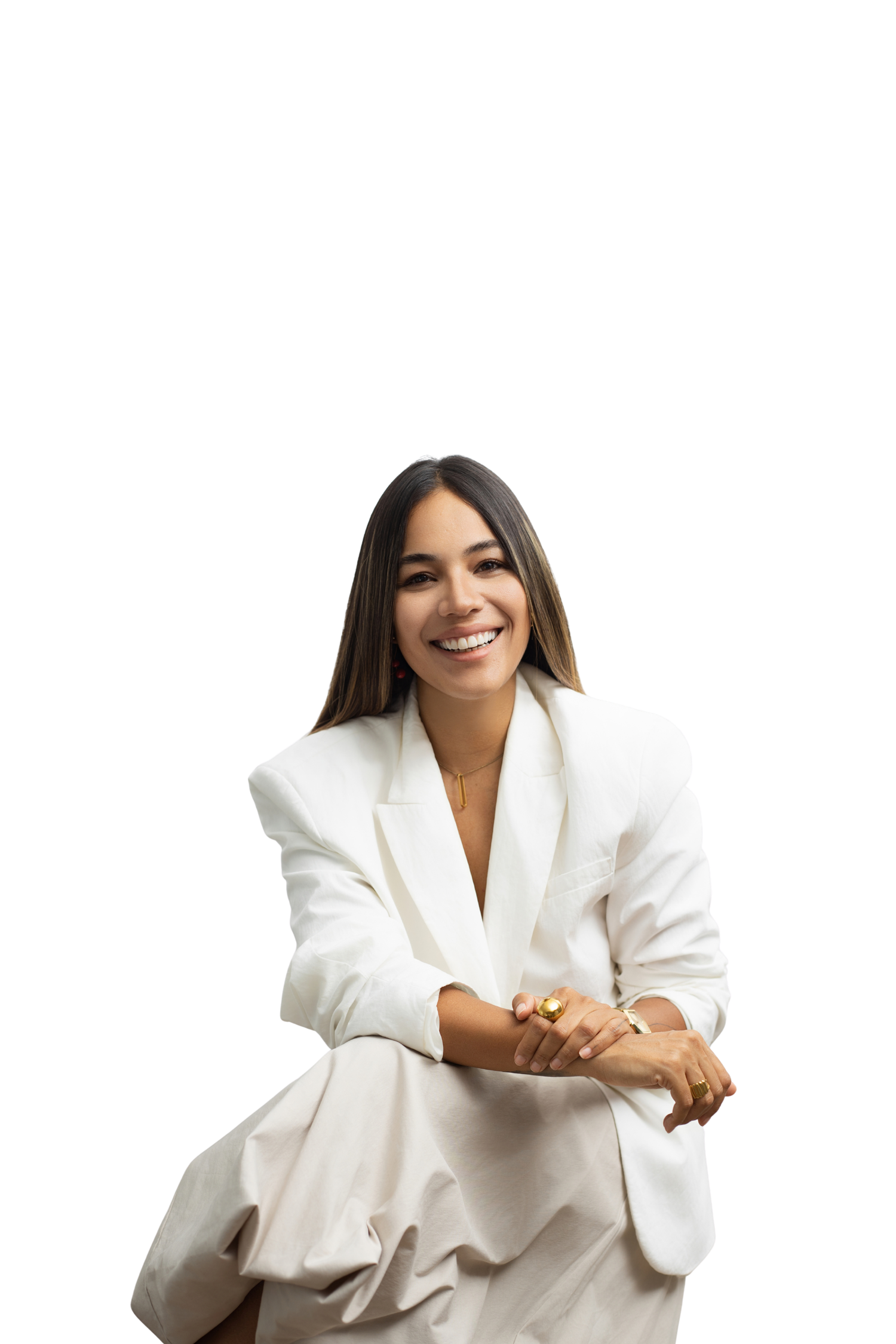 A smiling woman in a white blazer suit sits confidently with hands clasped, posing against a white background.