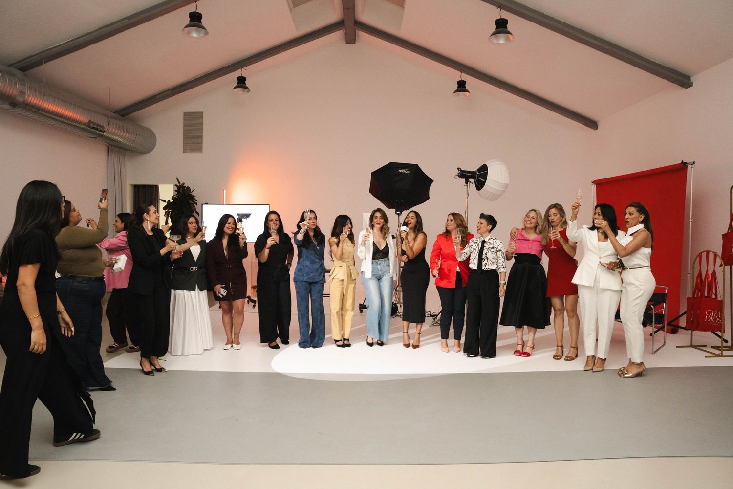 Group of elegantly dressed women posing together at a fashion event in a bright white venue.