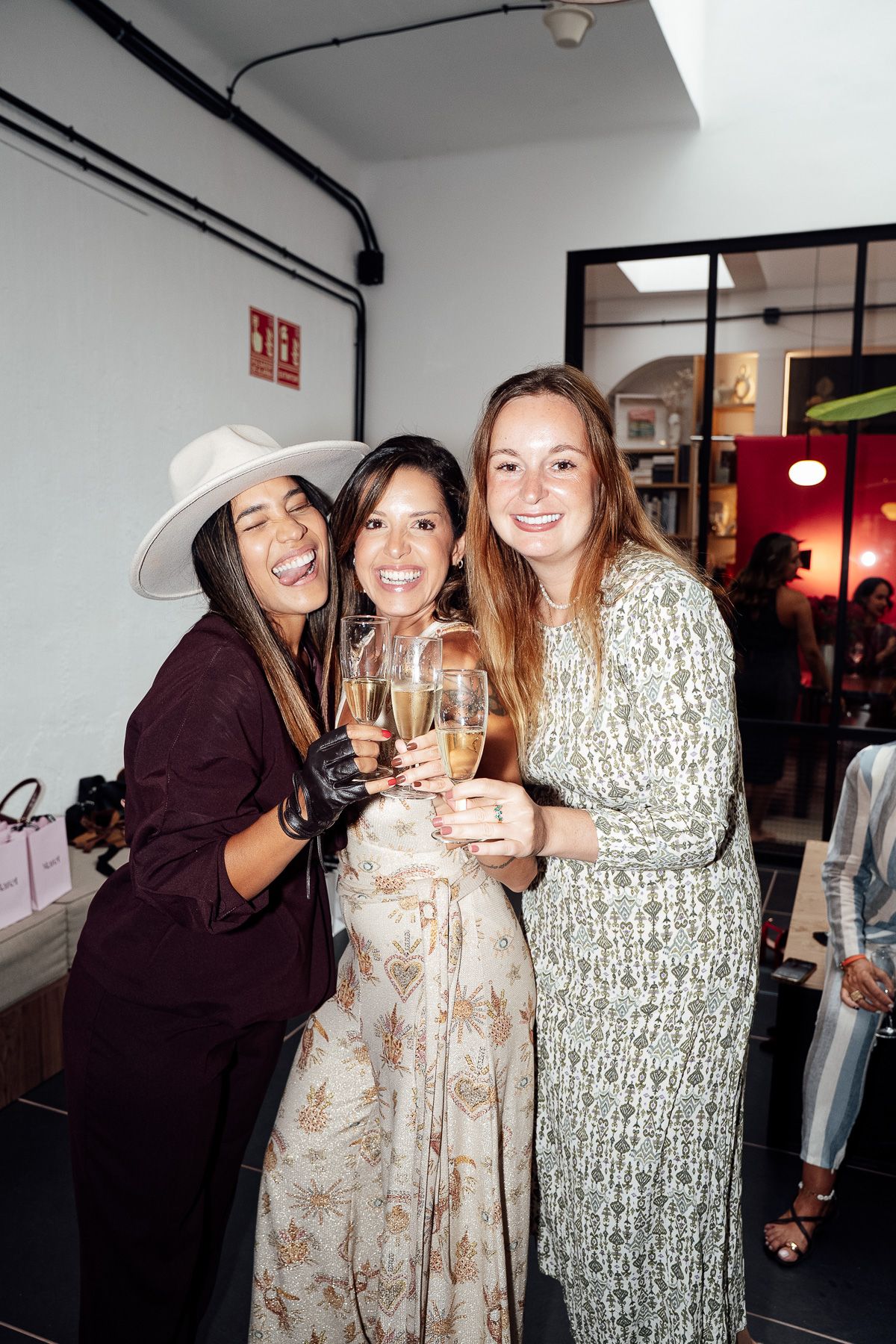 Three women smiling and toasting with champagne glasses at an indoor party event.