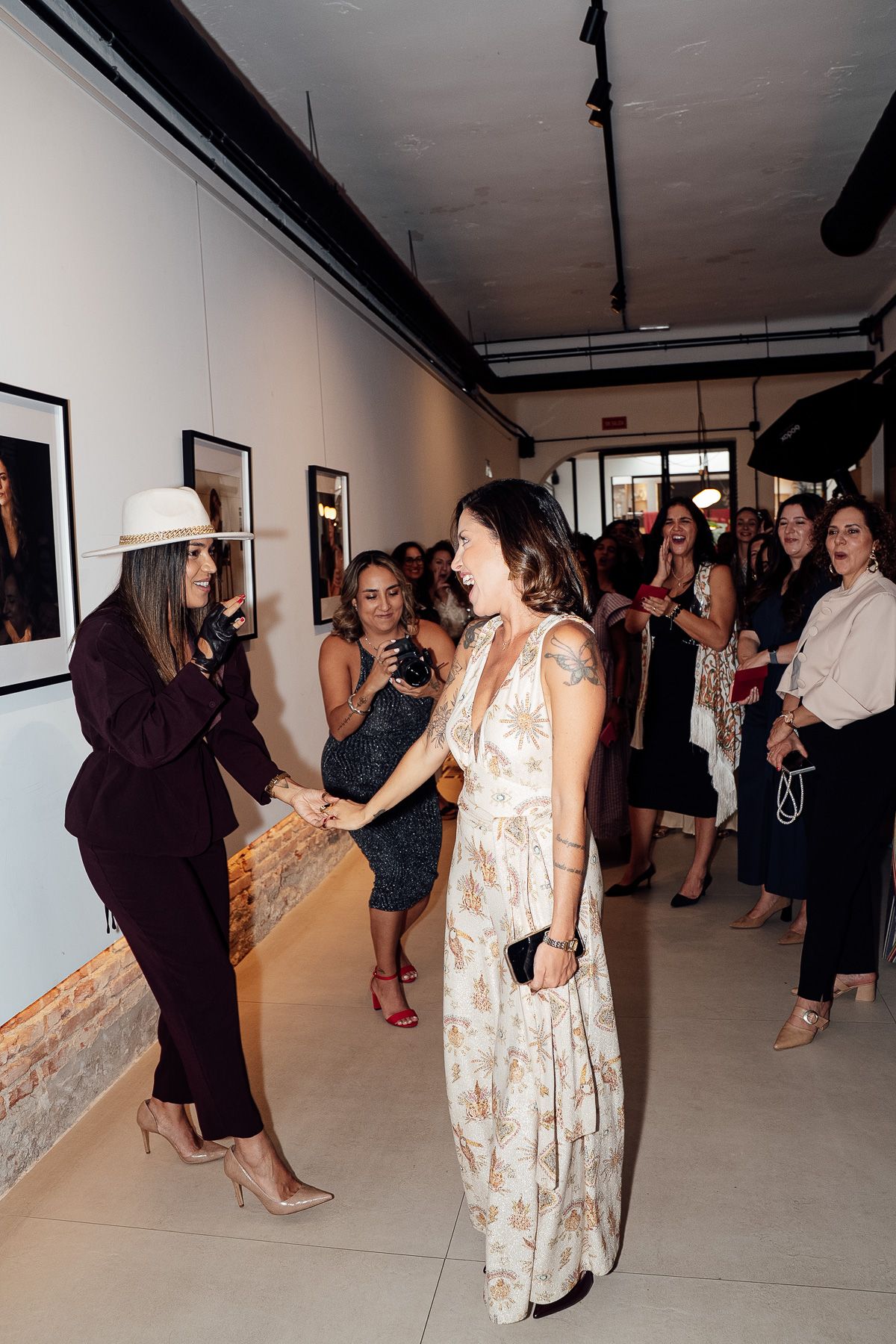 Woman in white hat greeting guest in floral dress at Gran Diosa gallery event.