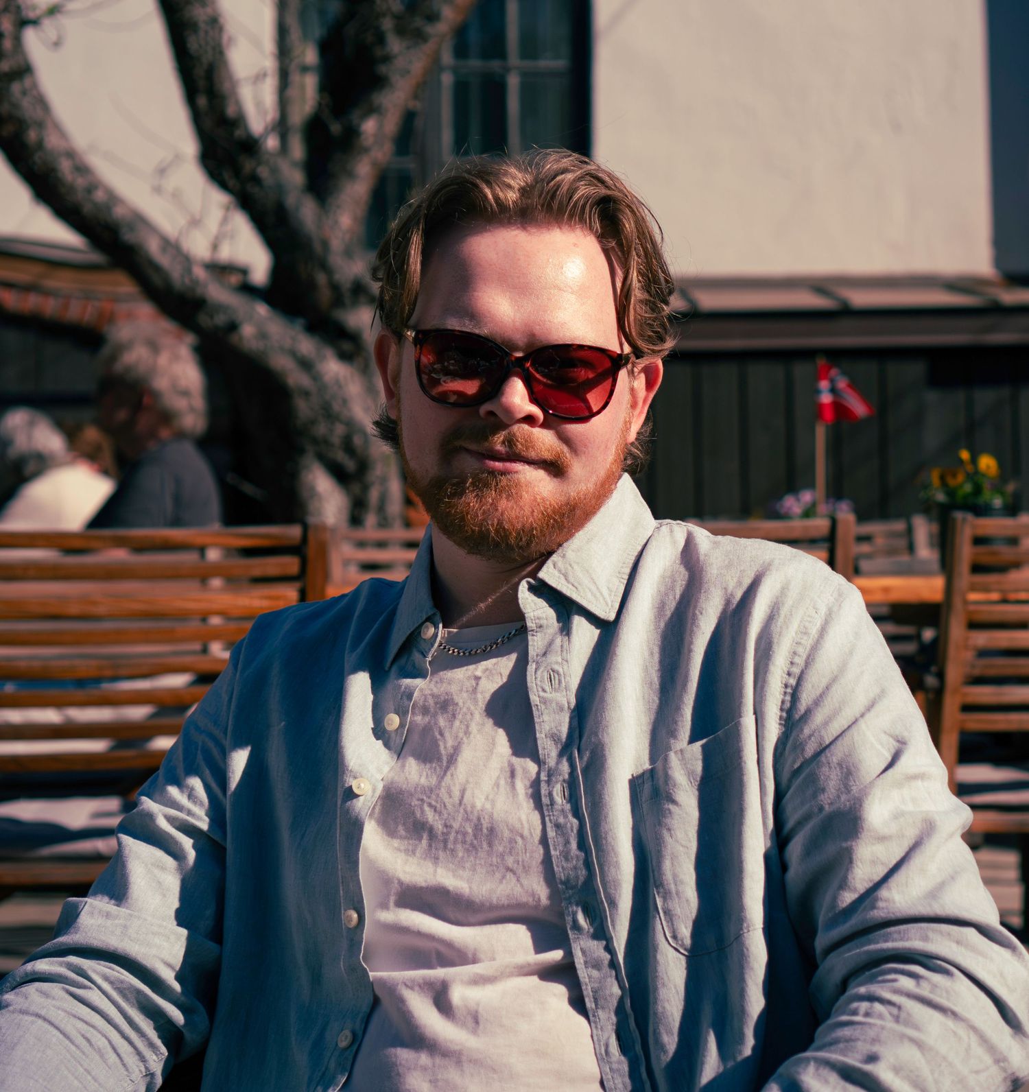 Bearded man wearing red sunglasses relaxing outdoors on a sunny day.