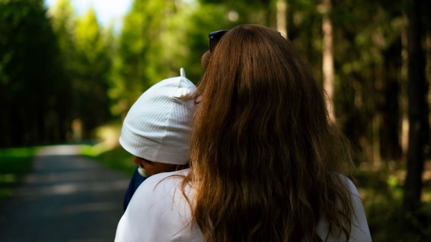 Two people walking on forest road surrounded by green trees.