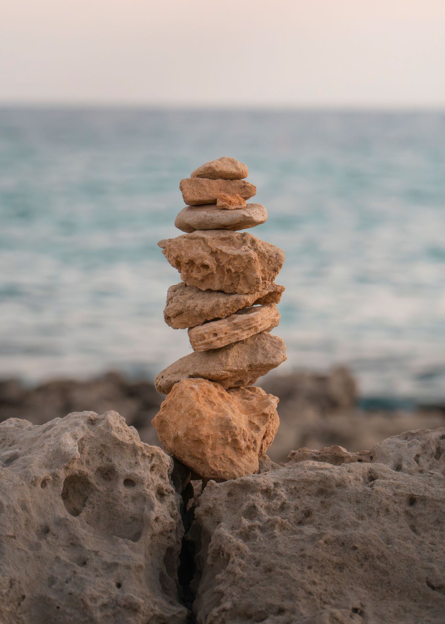 A balanced stack of smooth stones on rocky shore with calm blue ocean in the background.
