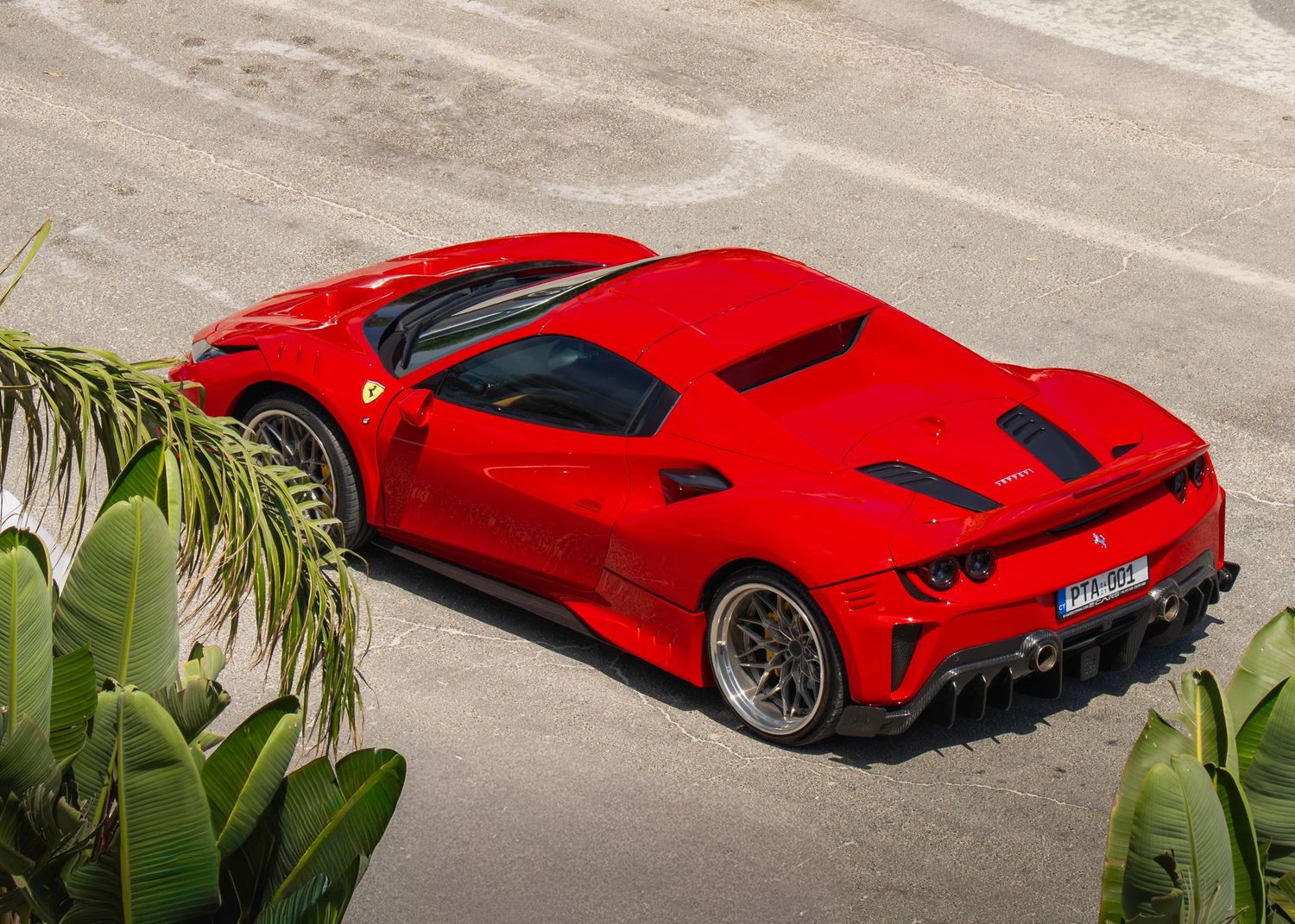 Red Ferrari supercar photographed from above, showcasing aggressive aerodynamic bodywork and carbon fiber details on a coastal road.