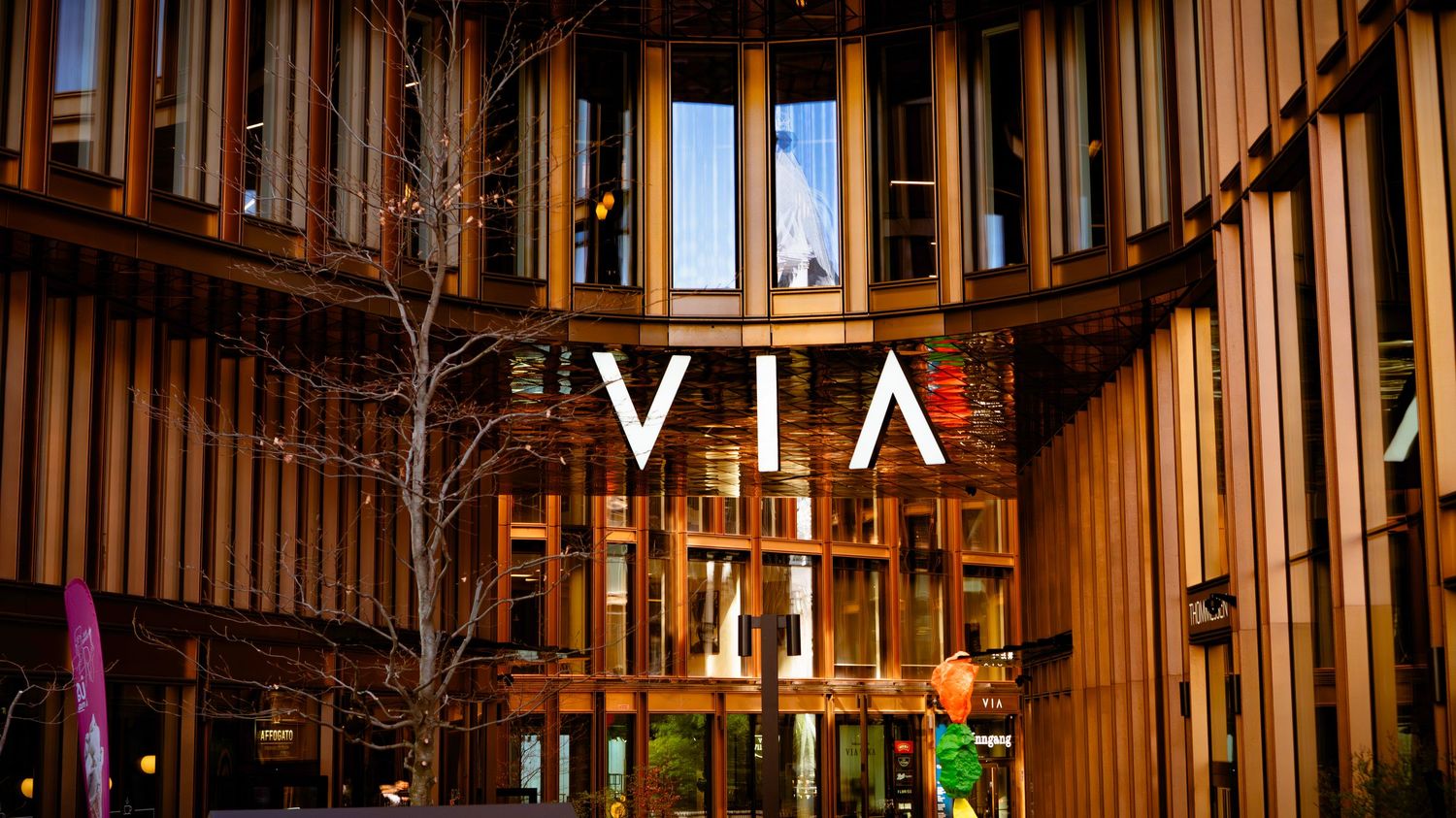 VIA building exterior featuring warm wooden slat facade with modern signage illuminated at dusk.