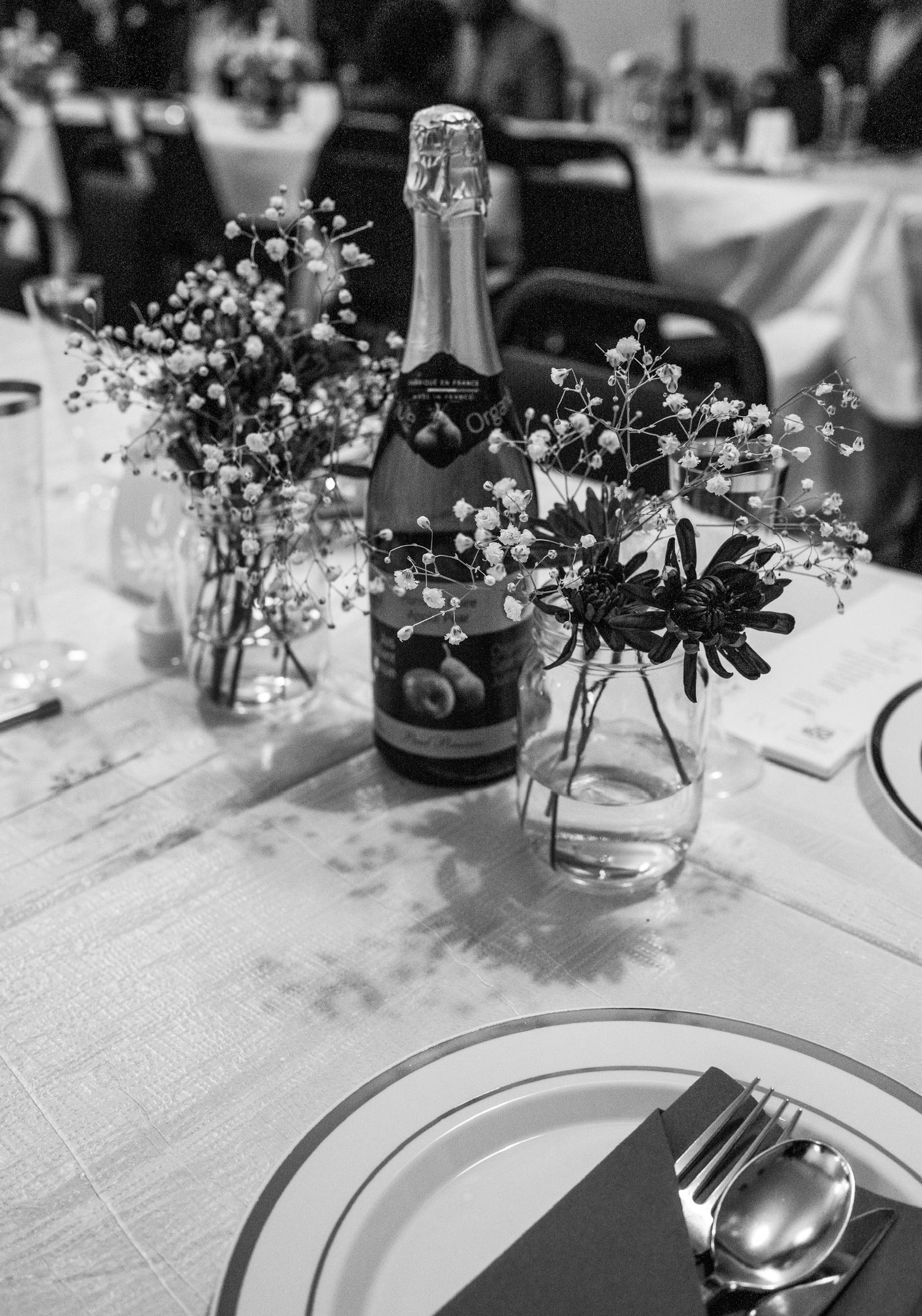 Black and white photo of an elegantly styled dining table with floral arrangement, champagne bottle, and place settings