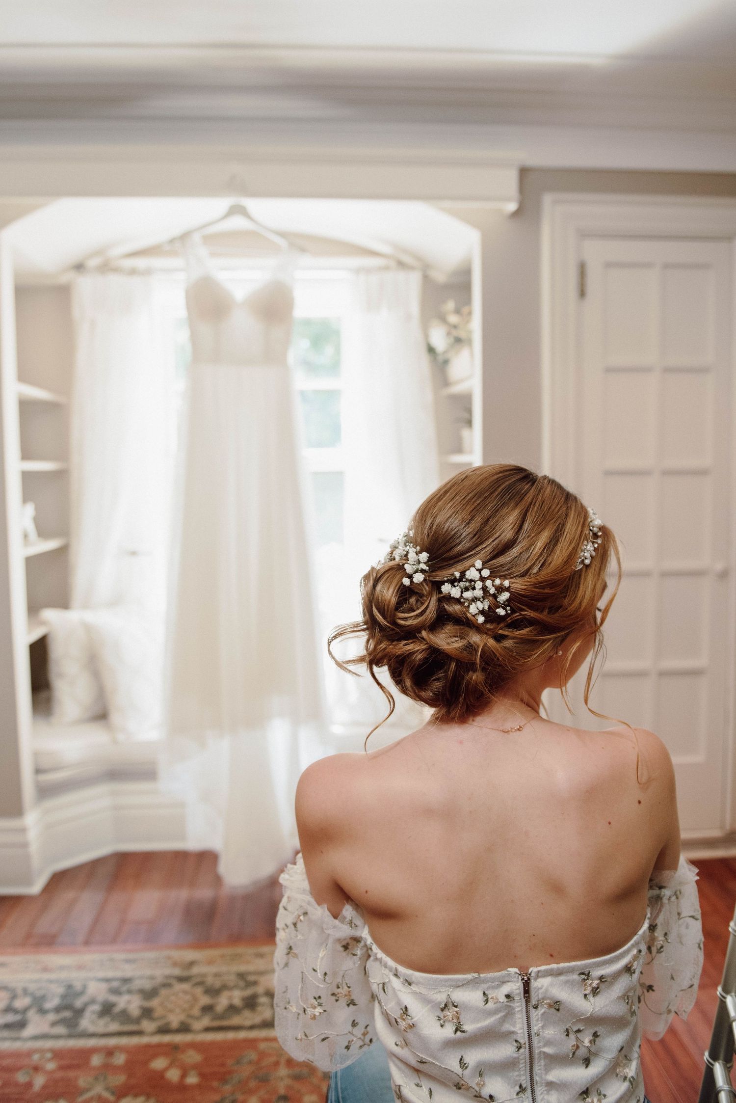 The bride in front of her wedding dress hanging in a window at Paletta Mansion