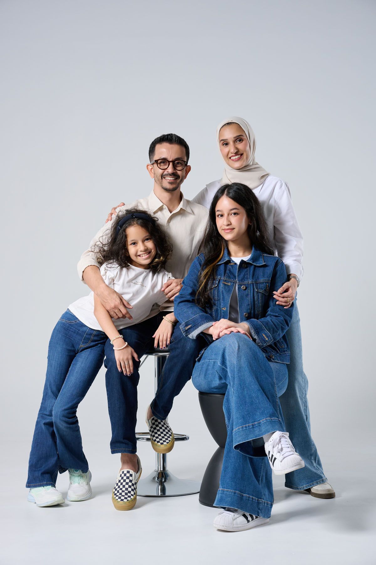 A smiling Muslim family of four posing together in coordinated denim outfits against a light gray studio background.