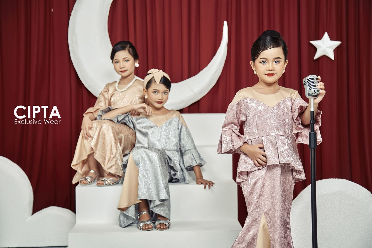 Three children in elegant Cipta Exclusive Wear baju kurung poses with crescent moon stage backdrop.