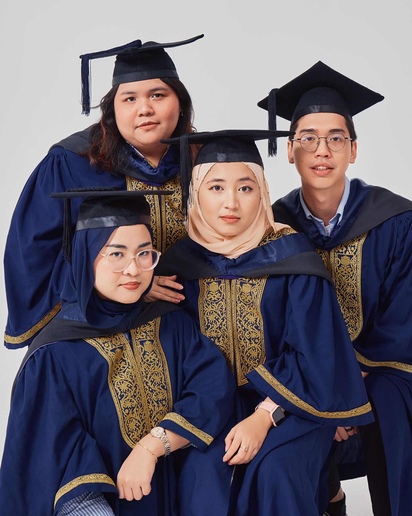 Four graduates in navy and gold robes with mortarboard caps smiling in a fun group portrait.