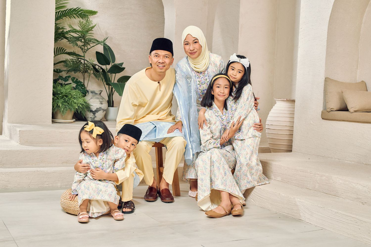 Muslim family in coordinating pastel traditional outfits sitting together for Hari Raya portrait.