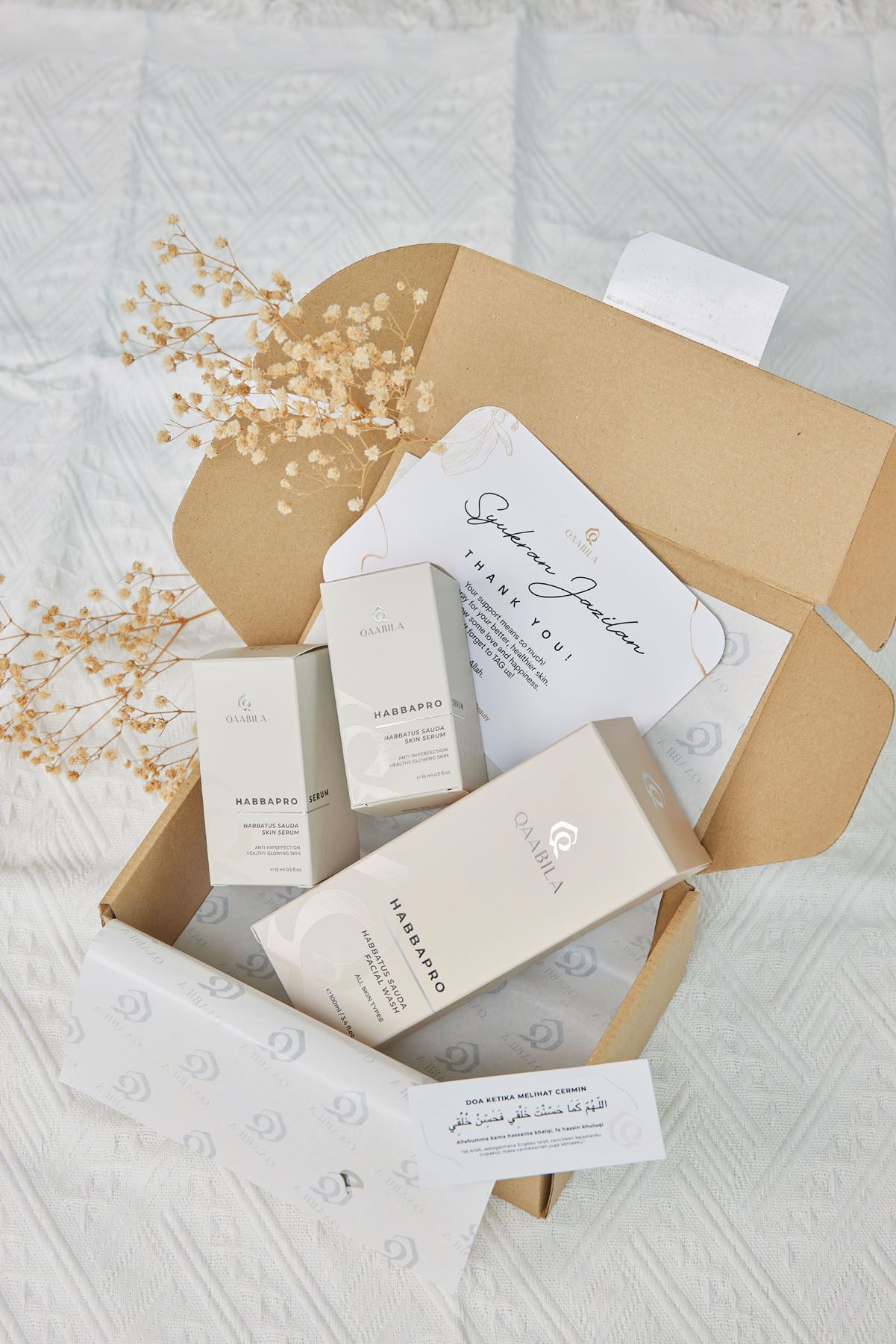Open kraft gift box containing white Harbardo skincare products with dried flowers and a personalized card.