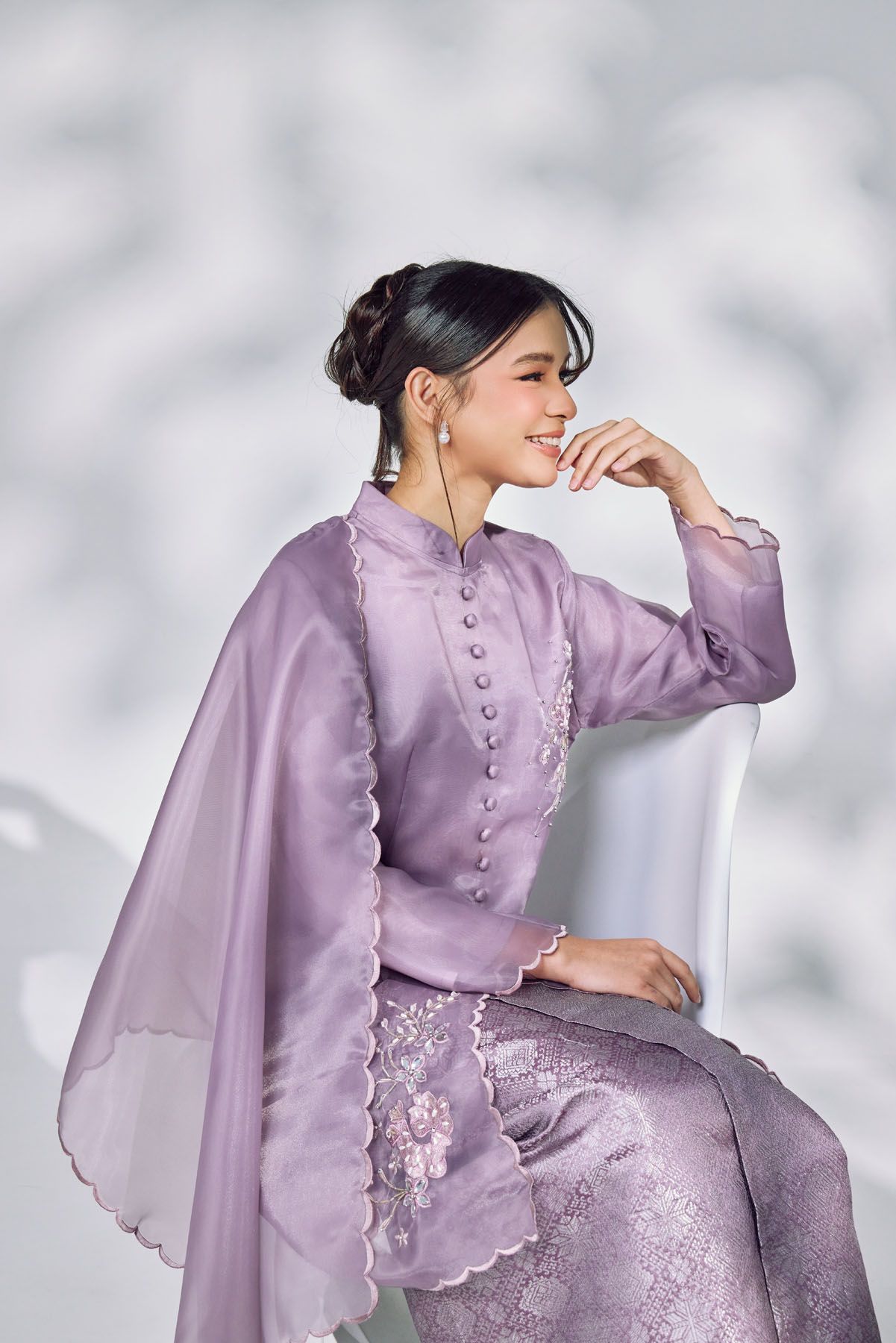 Woman in elegant lavender embroidered kebaya with matching skirt smiling in a softly lit studio.