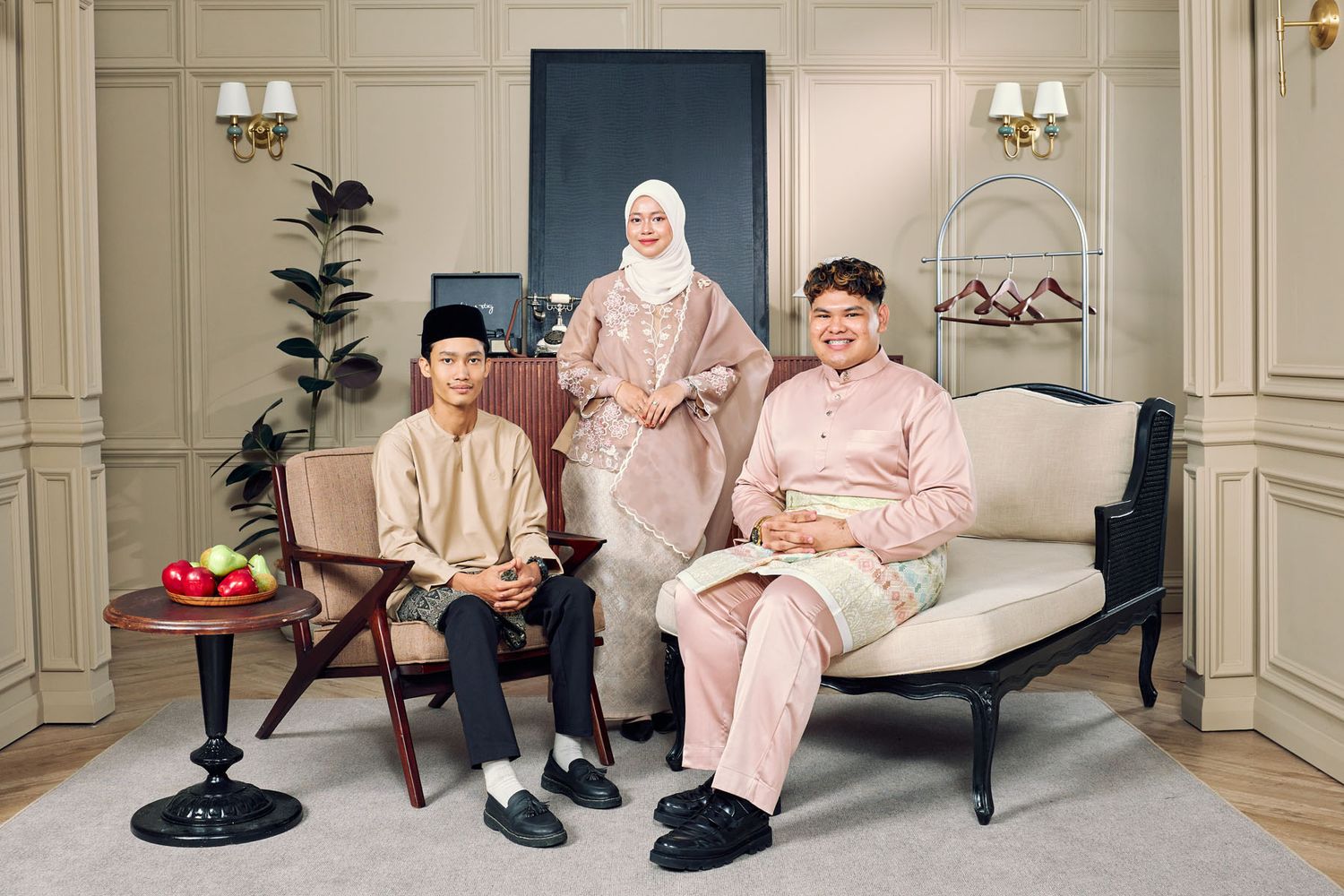 Family of three in matching blush pink traditional Malay attire seated in elegant cream interior setting.