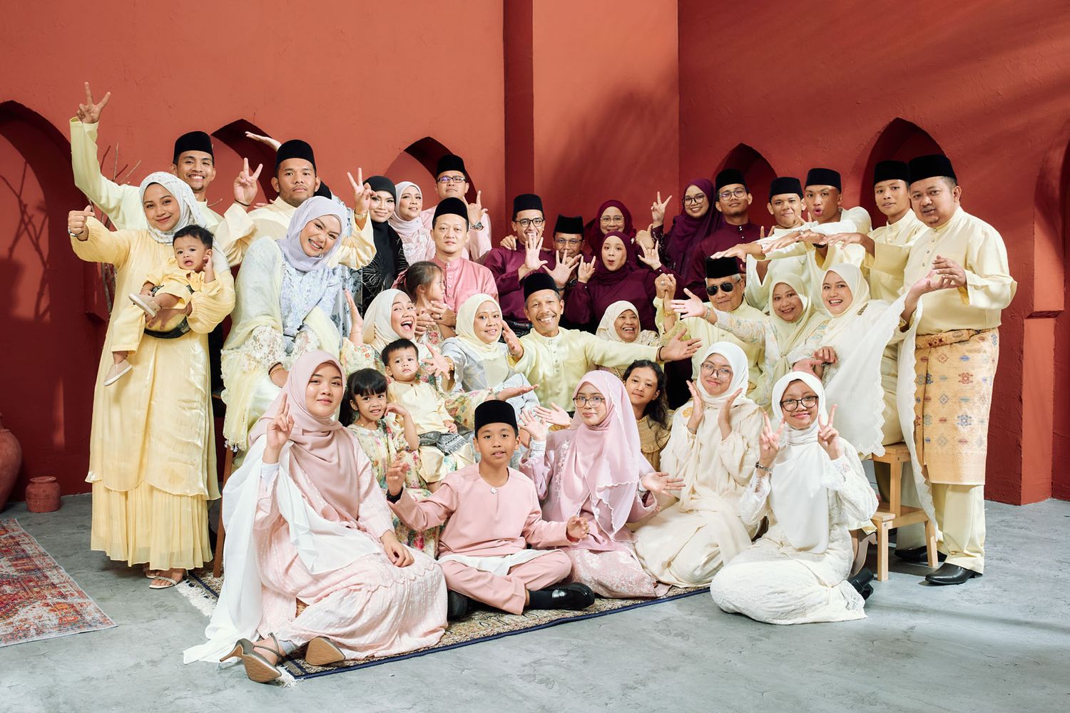 Large extended Malaysian family in matching cream and pink traditional Eid outfits group portrait.