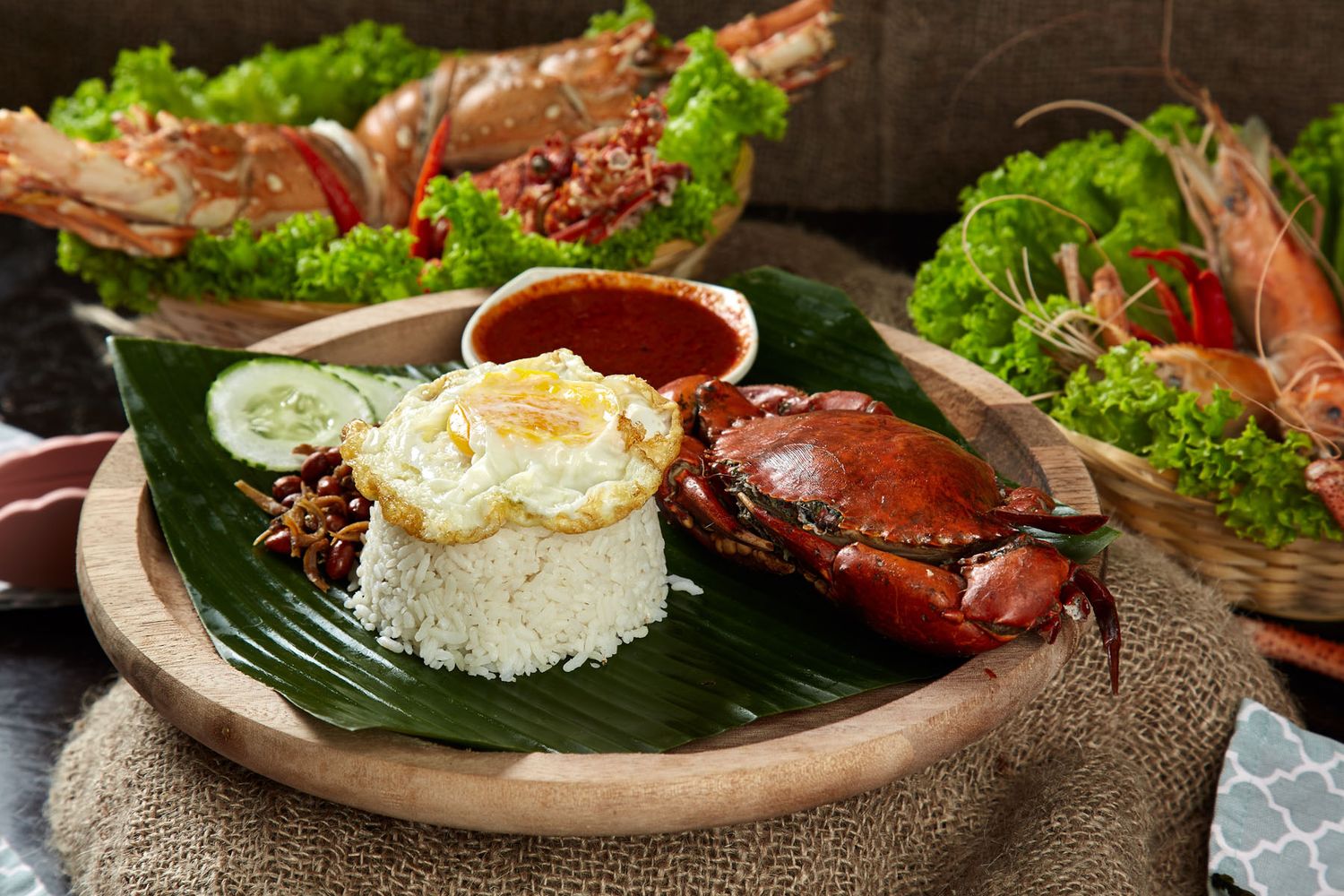 Fried rice with egg, crab, and shrimp served on banana leaf in wooden bowl with sambal sauce.