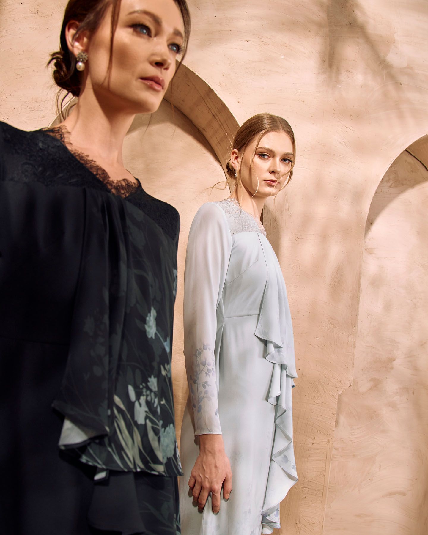 Two women in elegant modest black and powder blue dresses with ruffle details in desert setting.