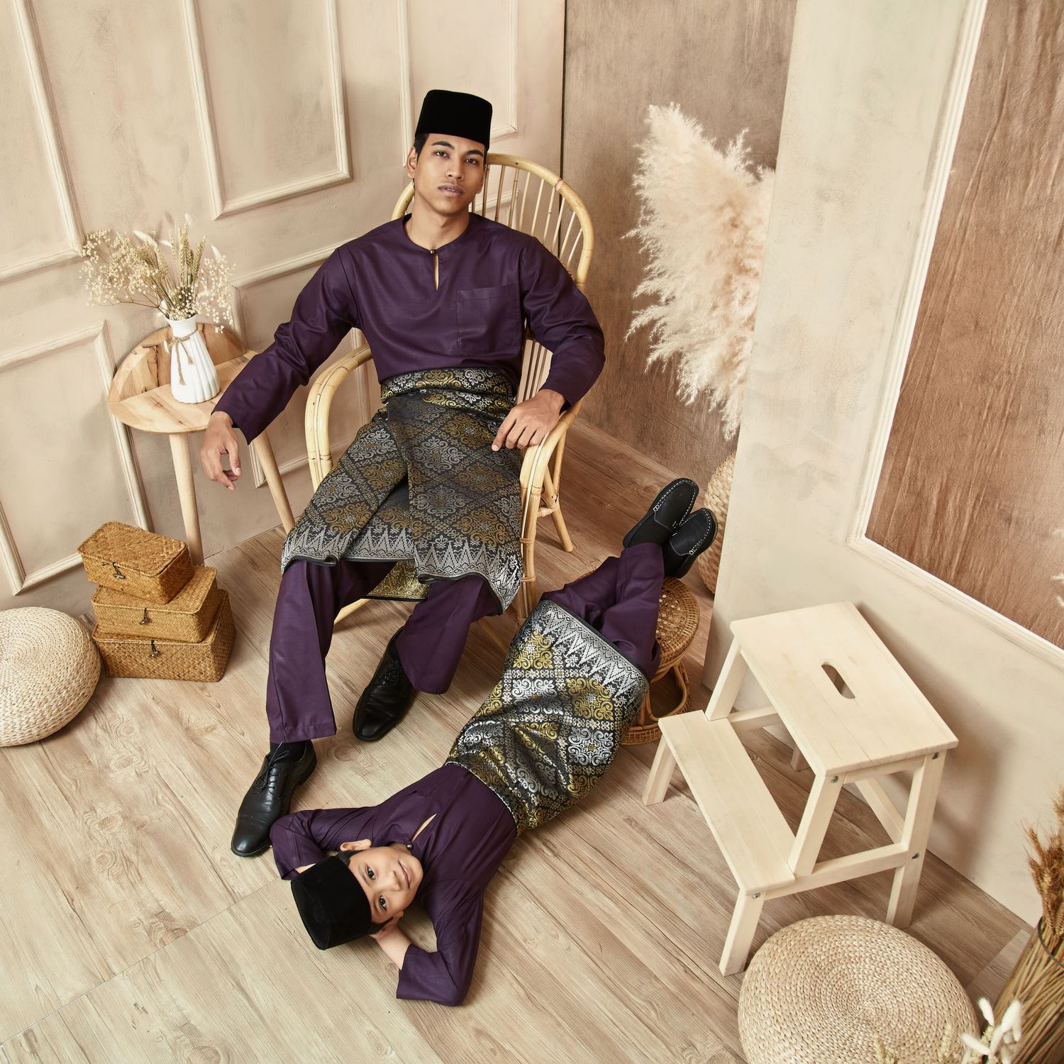 Man and boy in matching purple Baju Melayu with songket posing in a styled studio.
