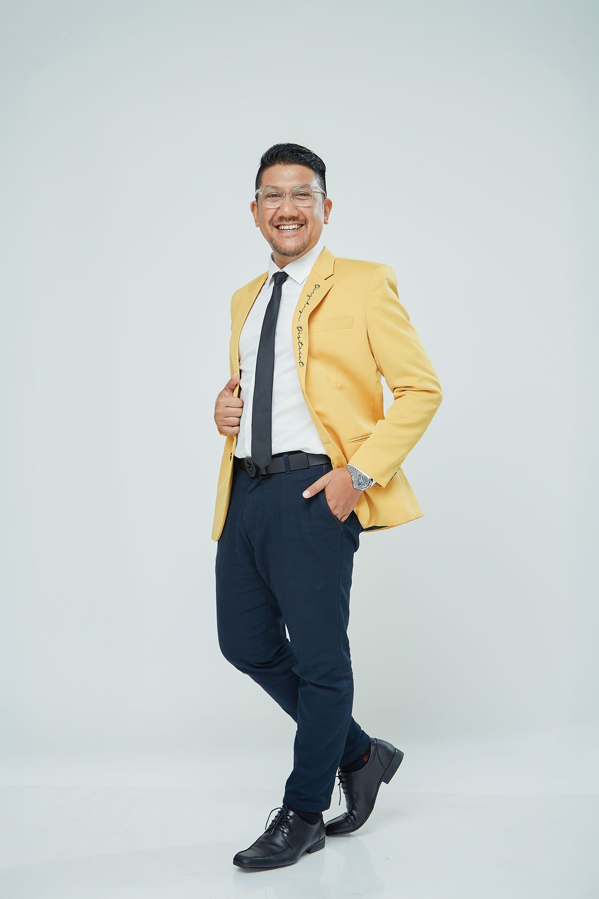 Smiling Asian man in yellow blazer and black tie posing confidently against white background.
