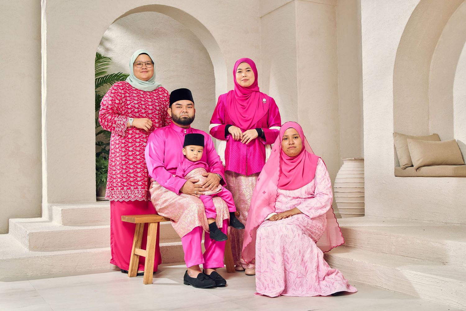 Malaysian family dressed in matching bright pink baju kurung and baju melayu for Eid festive portrait.