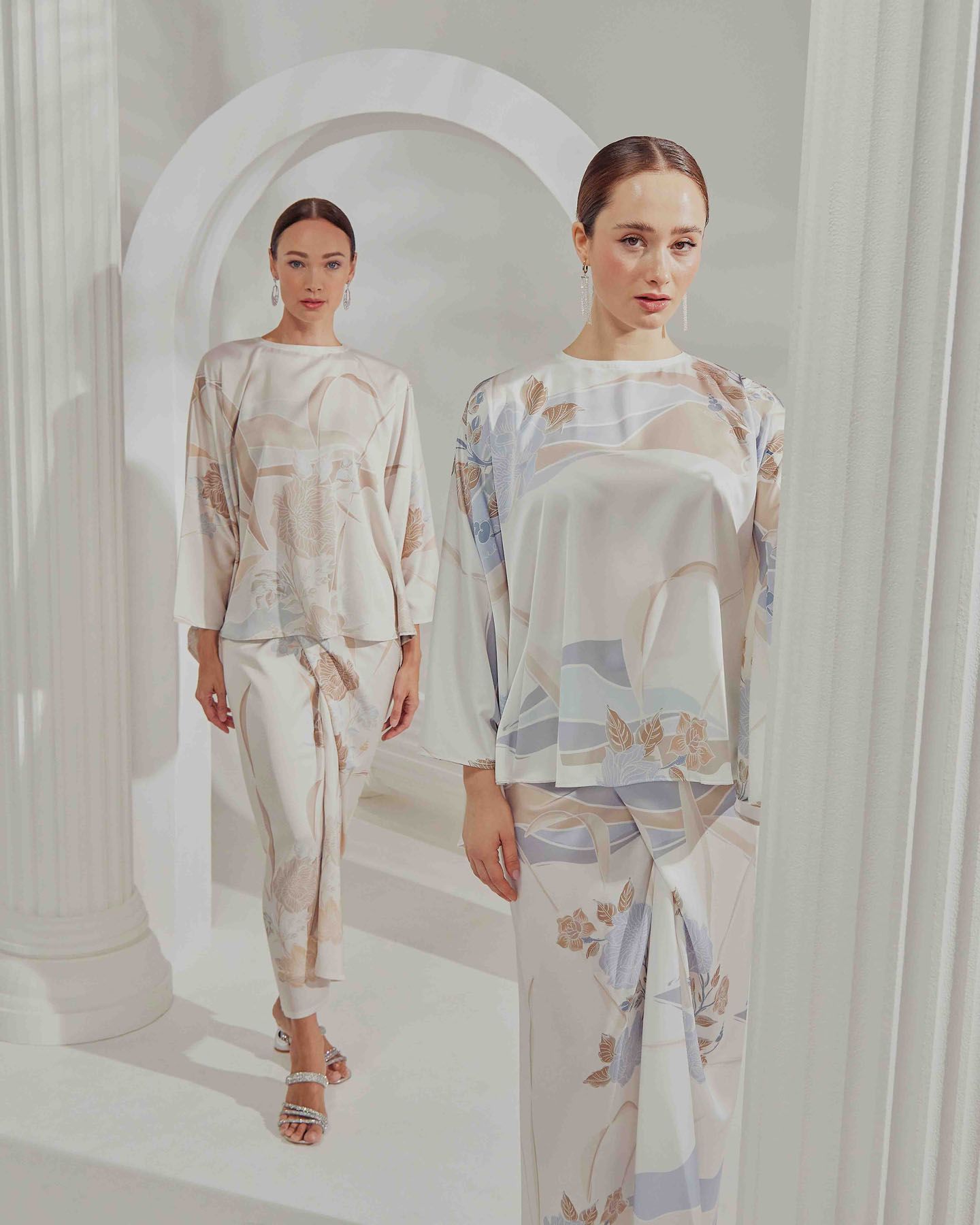 Two models wearing matching floral pastel printed modest fashion coordinates in elegant white architectural setting.