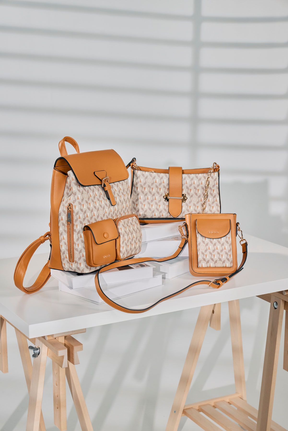 Matching tan and beige monogram bag set including backpack, crossbody, and phone bag on white table.