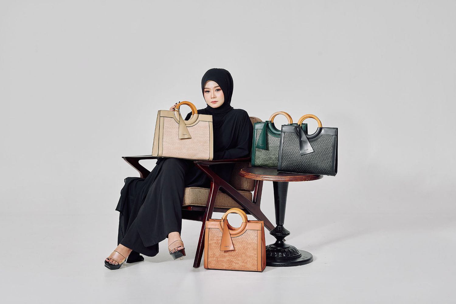 Woman in black abaya and hijab surrounded by collection of structured handbags on display.