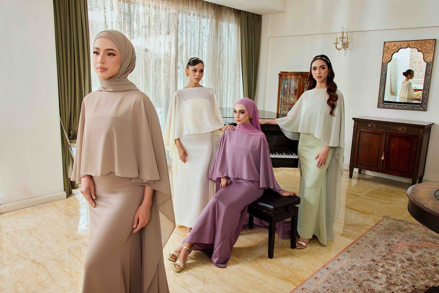 Four women in modest pastel hijab outfits pose together in an elegant room with a grand piano.
