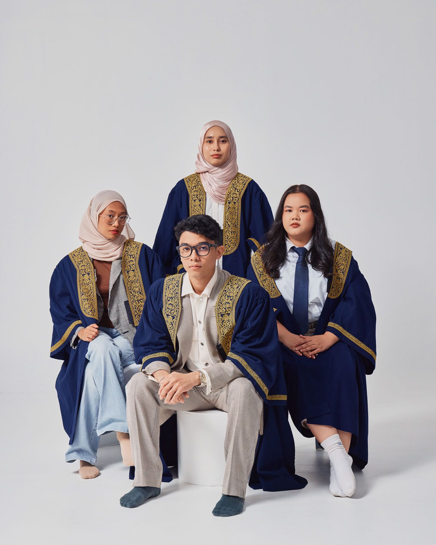 Four graduates in navy robes posing for a formal graduation portrait photo.