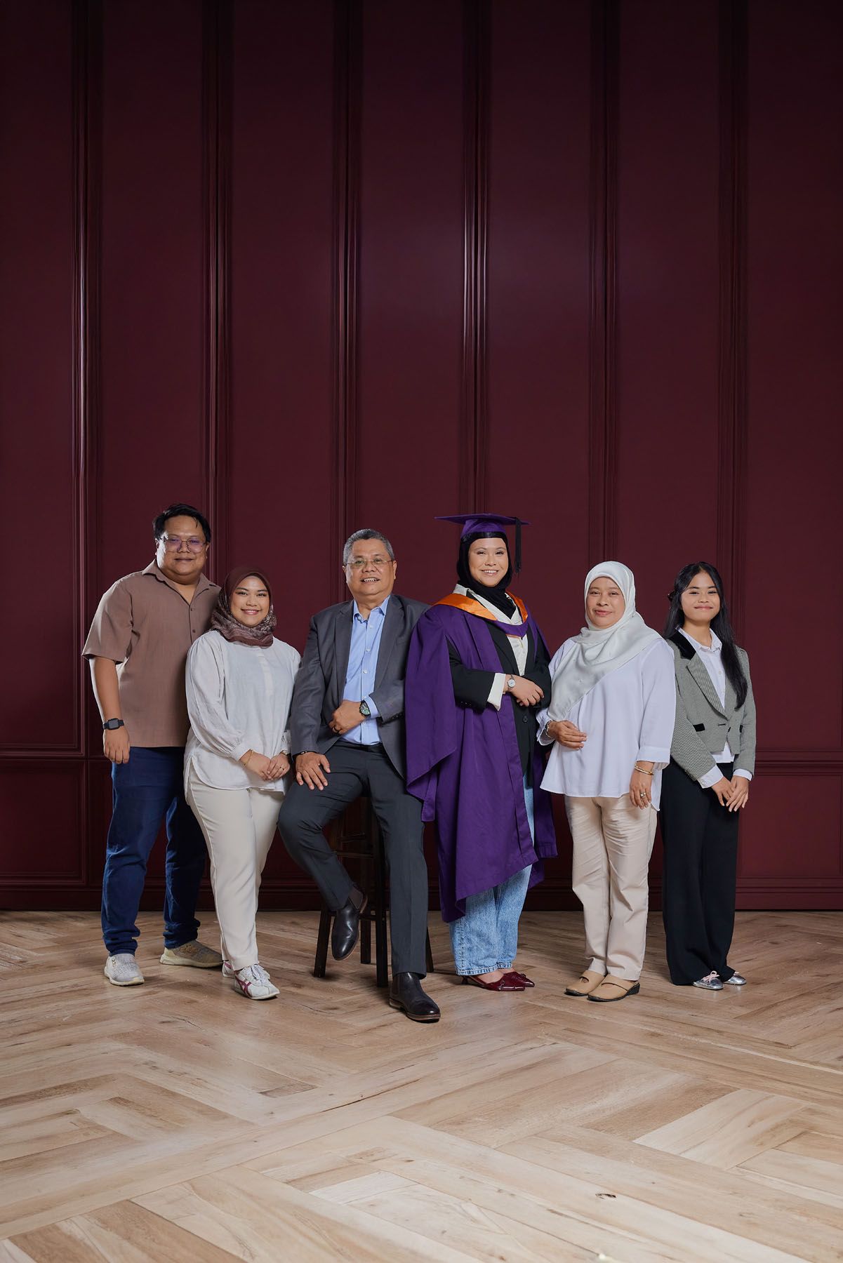 Group of six people posing with graduate in purple gown and cap in elegant red room.